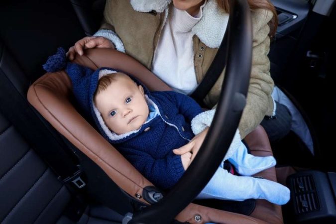 Un bébé vêtu de bleu est installé confortablement dans un siège auto, prêt à survivre aux trajets en voiture en toute sécurité.